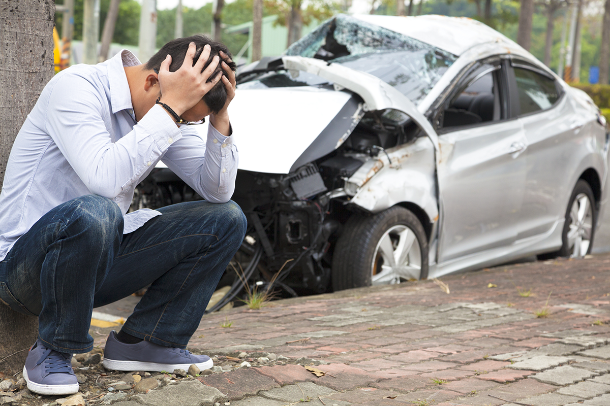 man with head in hands and a wrecked car in the background